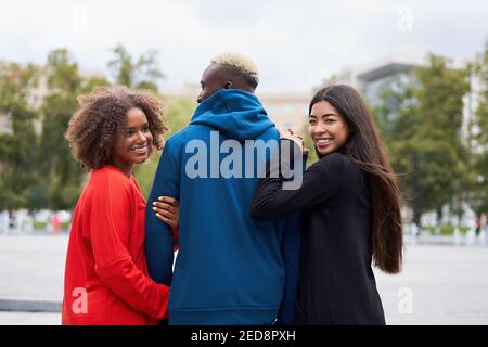 Multi ethnic friends outdoor. Two woman in love with one guy Diverse group people Afro american asian spending time together Multiracial male female student walking park outdoors Stock Photo