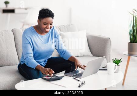 Black woman using calculator and laptop pc at home Stock Photo