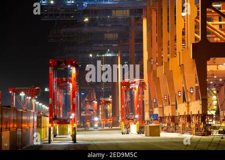 Cranes and containers in the container harbour port during logistic loading process at night time with artificial lights during work Stock Photo