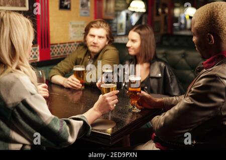 Several young intercultural friends sitting by table in pub, having beer and discussing their plans and ideas for forthcoming saint patrick day Stock Photo