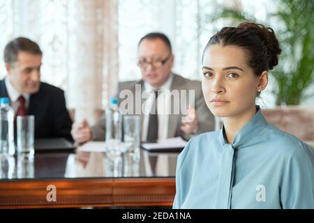 Young brunette secretary in smart casualwear looking at you while standing against two mature business delegates or partners Stock Photo