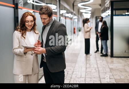 Caucasian business partners at the workplace. Friendly colleagues cooperate to develop a startup or project together. Handsome man ask for advice from beautiful smiling woman, collaboration concept Stock Photo