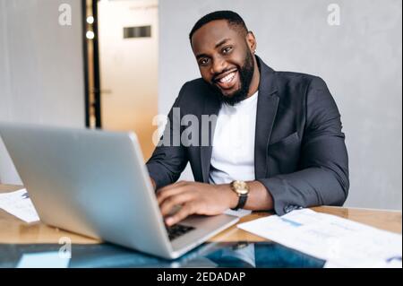 Portrait of african american business man at the workplace. Successful male manager using laptop, work on new project or startup. Handsome confident employee look at the camera, smiling Stock Photo