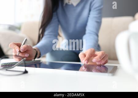 Female hand on tablet with second hand makes notes with pen in notebook Stock Photo