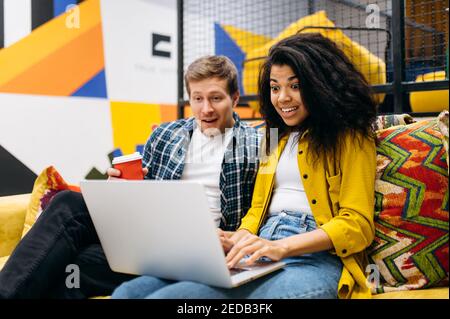 Joyful business coworkers sitting in office, surprised look at the laptop screen, smiling. Successful colleagues happy about work project. Young adult students get good mark, well done with passing Stock Photo