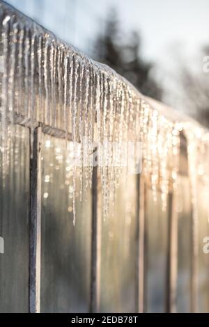 Sharp icicles on the roof of greenhouse in sunny winter day on the sunny side Stock Photo