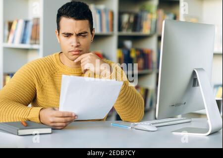 Serious business male sits at the table in office, doing some paperwork. Focused employee looking at documents, working with financial statements Stock Photo