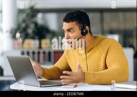Attractive hispanic young man student or coworker surprised looks at laptop while working or studying online Stock Photo