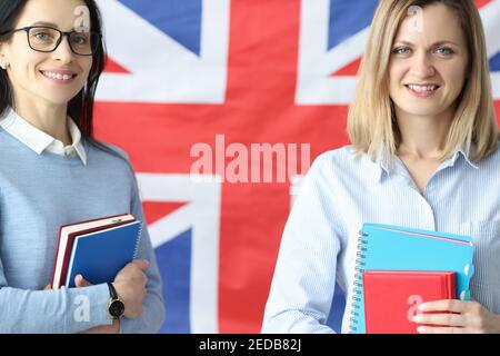 Two smiling women stand with notebooks in front of British flag Stock Photo