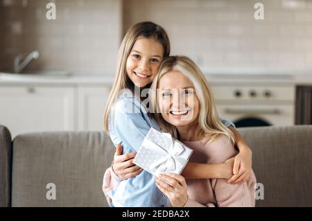 Happy caucasian grandma and granddaughter. Portrait of cheerful granddaughter with her middle aged beloved grandma, hugging at home on the couch and smiling Stock Photo
