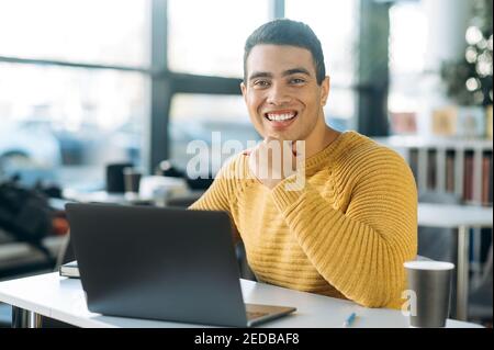 Portrait of happy successful business man at the workplace. Joyful hispanic male freelancer or student sit at the work desk in office, look directly at the camera and smiling Stock Photo