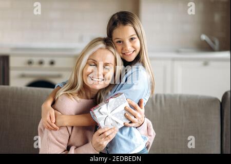 Happy caucasian grandma and granddaughter. Portrait of cheerful granddaughter with her middle aged beloved grandma, hugging at home on the couch and smiling Stock Photo