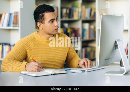 Concentrated business person working online. Hispanic male freelancer search ideas browsing internet. Focused employee sit at the desk in office, works remotely Stock Photo