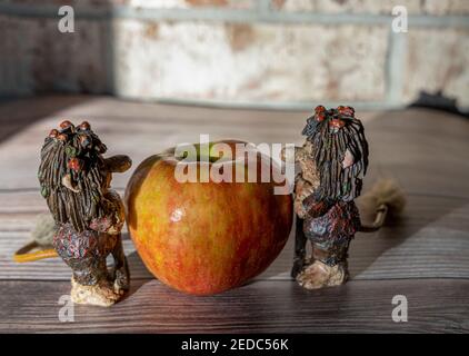 Big red apple and funny trolls figures on the wooden table against the brick wall Stock Photo