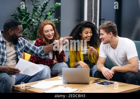 Friendly multiracial business colleagues sitting in office, talking about work process, smiling. Coworkers communicate with each other, discuss about new startup. Cheerful students learning together Stock Photo