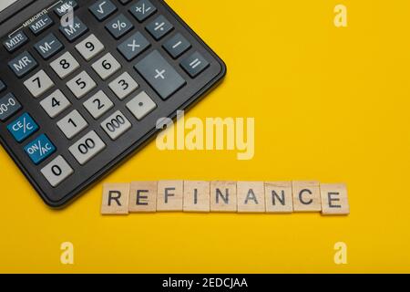 Phrase or word - refinance. Wooden block letter word and modern calculator on a yellow background, business concept with space for text Stock Photo