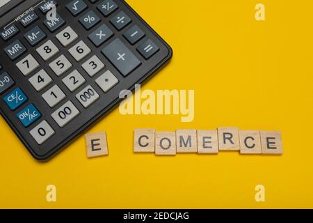 Phrase or word - e-comerce. Wooden block letter word and modern calculator on a yellow background, business concept with space for text Stock Photo