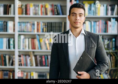 Portrait of hispanic man in formal wear at the workplace. Successful male manager looks at the camera, smiling. Influential businessman standing in modern office, show self confidence Stock Photo