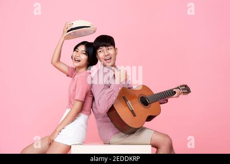 Happy young Asian man playing guitar and singing with his girlfriend studio shot on pink background Stock Photo