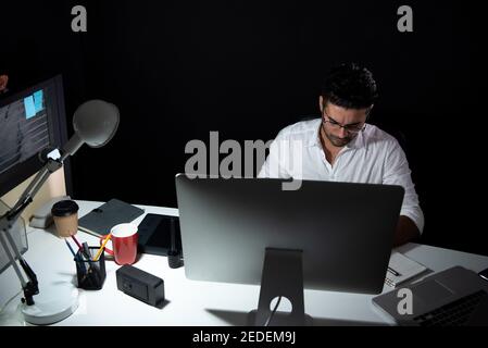 Asian businessman staying overtime late at night in the office concentrating on working in front of computer Stock Photo
