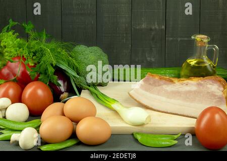 Fresh chicken eggs and balyk with vegetables are laid out on the table. On the table are products for the eggs with bacon and vegetables. Space for te Stock Photo