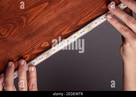 the master glues the LED strip into the niche of the shelf from the cabinet for lighting.installation of diode lighting tape Stock Photo