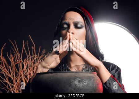 Evil young witch performing ritual on dark background Stock Photo