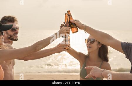Group of friends having celebration party claging beer bottles making a toast before drinking at the beach in twilight Stock Photo