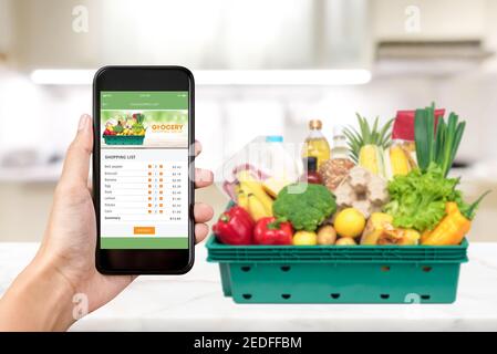Grocery online shopping application on smartphone screen with food at home in background Stock Photo