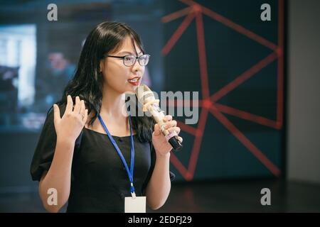Asian woman standing and speaking at event. Stock Photo