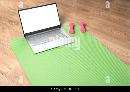 online yoga fitness, laptop mockup. Pink dumbbells, gym mat and grey laptop on wooden floor. Online workout concept. copy space. watching online yoga Stock Photo