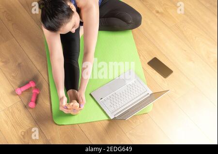 Online Laptop Yoga Home. Top view of woman practicing yoga on yoga mat with laptop. middle aged woman is meditating and relaxing with video training a Stock Photo