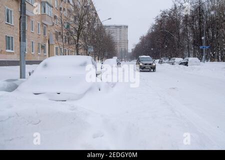 Moscow. Russia. February 13, 2021. Cars parked along the road on a winter day are covered in a thick layer of snow after a heavy snowfall. Stock Photo