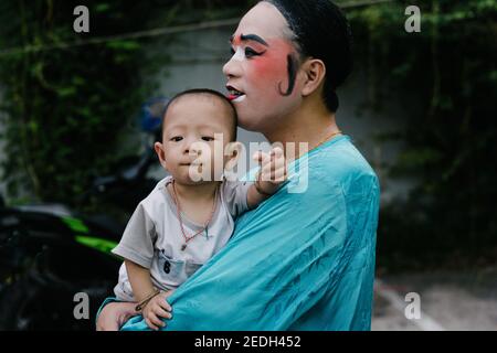 Chinese opera player holds his baby boy while waiting backstage to get dressed in his costume. Stock Photo