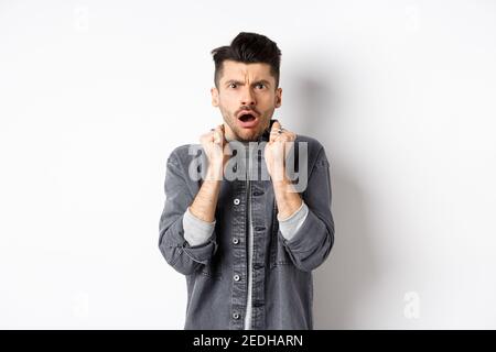 Shocked young man look confused and offended, gasping and frowning at camera, hear bad news, standing on white background Stock Photo