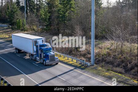 Powerful Big rig industrial classic blue semi truck tractor transporting frozen commercial cargo in refrigerated semi trailer running for delivery on Stock Photo