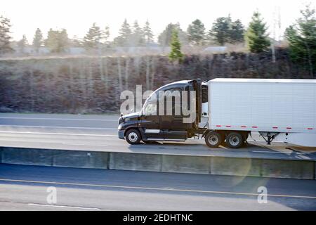 Powerful Big rig industrial classic black semi truck tractor transporting frozen commercial cargo in refrigerated semi trailer running for delivery on Stock Photo