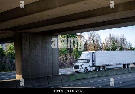 Big rig industrial white day cab semi truck tractor transporting frozen commercial cargo in refrigerated semi trailer running for delivery on the wide Stock Photo