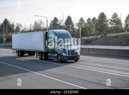 Big rig industrial green classic American semi truck tractor transporting frozen commercial cargo in refrigerated semi trailer running for delivery on Stock Photo