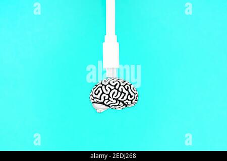 White data cable attached to a small steel copy of a human brain isolated on a blue background. Creative education and knowledge transfer concept. Stock Photo