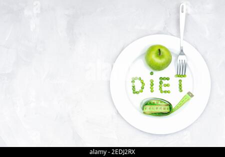 Word DIET made of garden peas on a large white plate with a fresh green apple, a soft tape measure and a fork on a concrete table. Healthy lifestyle, Stock Photo