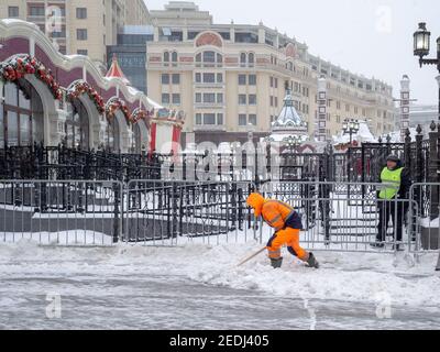Moscow. Russia. February 12, 2021. A utility janitor in orange uniform shovels snow on a city street during a heavy snowfall on a winter day. Abnormal Stock Photo