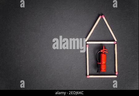 Small house made of matches with a miniature fire extinguisher inside. Business fire insurance concept. Stock Photo