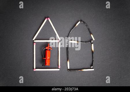 Two houses made of burnt and unburnt matches with a miniature fire extinguisher inside the undamaged one. Fire safety measures and insurance concept. Stock Photo
