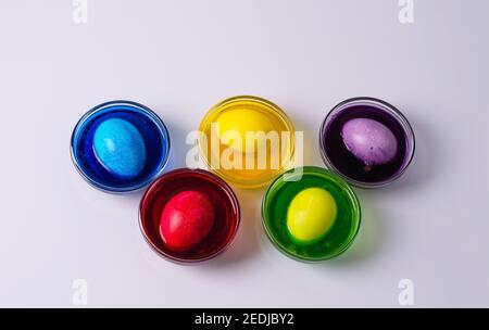 Chicken white eggs lie in glass bowls with colored water on a light background. Colors yellow, red, purple, green, blue. Step 4 Stock Photo