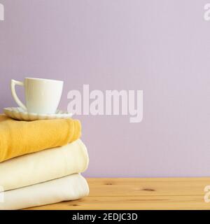 Stack of folded clothes and cup of coffee on wooden table. purple background. copy space Stock Photo