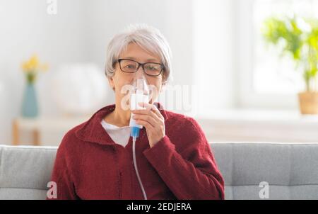 Elderly woman using inhaler for asthma and respiratory diseases at home. Stock Photo