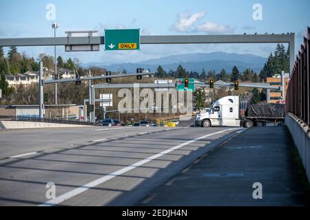 Big rig white classic semi truck tractor transporting covered commercial cargo on flat bed semi trailer turning on the city street with traffic lights Stock Photo
