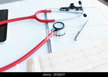Stethoscope and electrocardiogram lying on patients medical history closeup