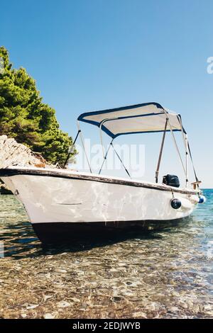 White boat with a canopy on the waves near the shore - transparent sea wave - boat at anchor Stock Photo
